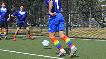 Person kicking soccer ball wearing rainbow socks
