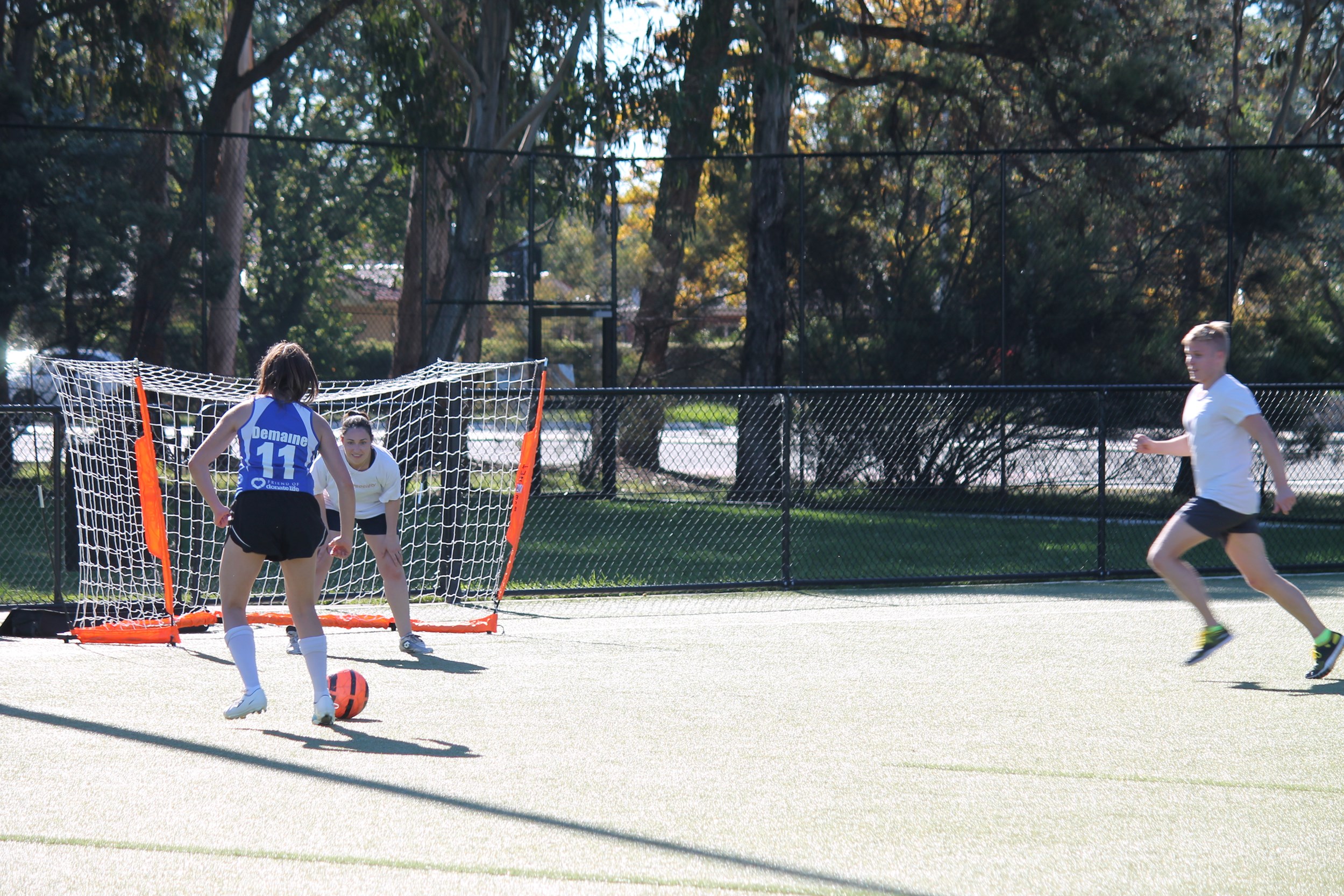 Women in blue singlet shooting the ball towards an orange goal 